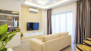 A modern living room with a sofa, television, and decorative items on shelves. - Villa Novaworld Phan Thiet - Elity (Tien Thanh)