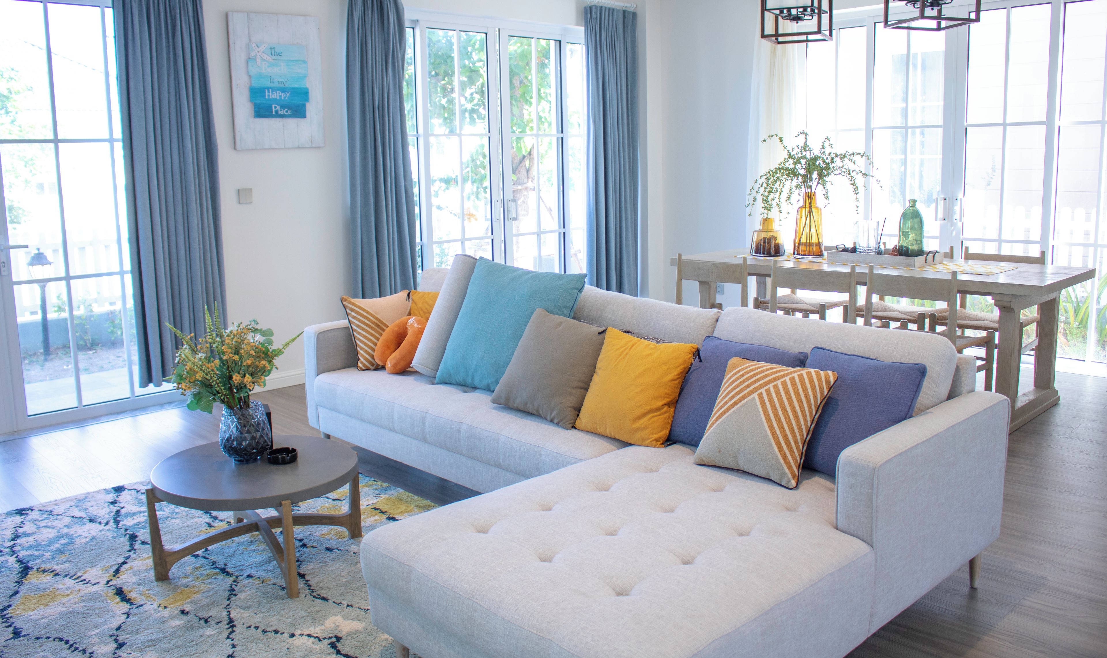 A modern living room with a sofa, a dining table, and a large window with curtains.