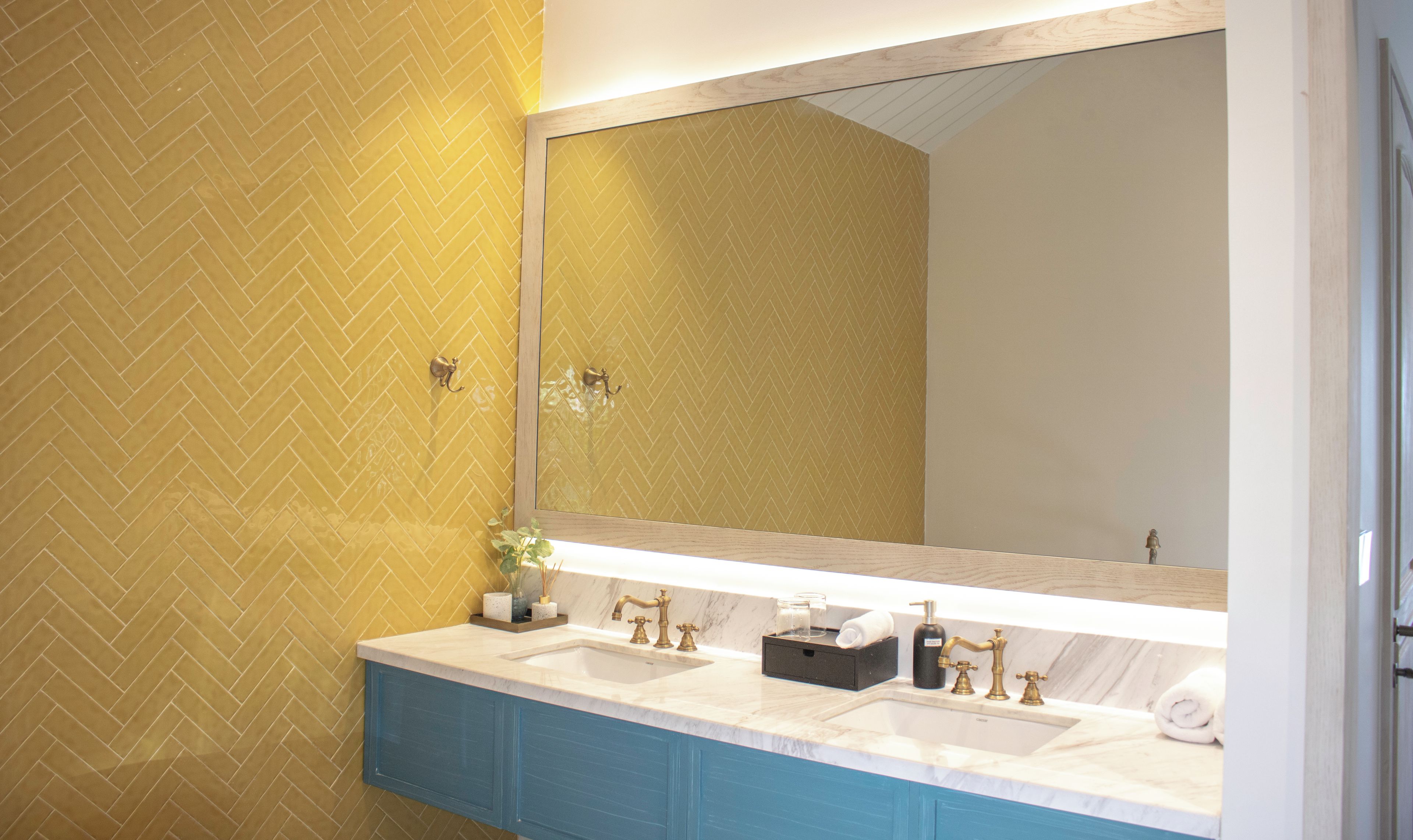 A bathroom with a herringbone-patterned wall, a large mirror, dual sinks, and a blue vanity.