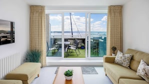 Sala de estar con sofá, una mesa de centro con planta, televisor y vistas a un balcón con mobiliario exterior.