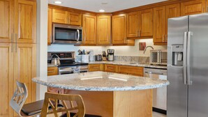 A kitchen with wooden cabinets, a stainless steel refrigerator, a microwave, a stove, and a granite countertop. - Summer Deal Updated 2BR Kona Condo Near Ocean and Downtown Kona (Kailua-Kona)