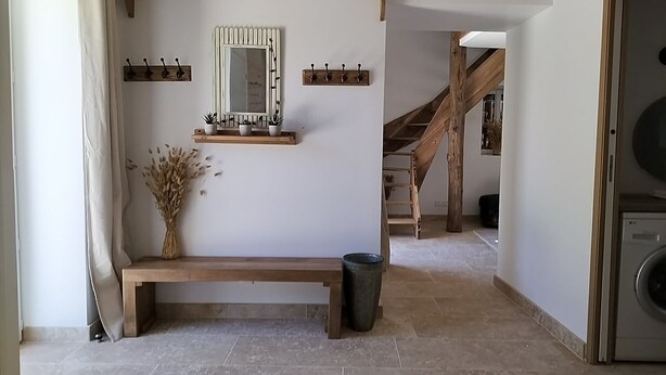 Un pasillo con un banco de madera, un espejo, ganchos para abrigos y una escalera.