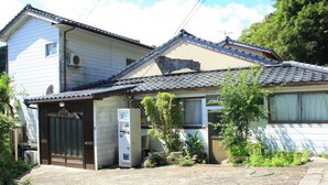 Ein traditionelles japanisches Haus mit einem Ziegeldach, einem kleinen Garten und einer Verkaufsmaschine.