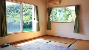 Ein Zimmer mit Tatami-Boden, zwei Fenstern mit Vorhängen und einer Fernbedienung auf dem Boden.