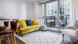 Una sala de estar moderna con un sofá amarillo, una mesa de comedor con sillas y un ventanal con vistas a edificios.