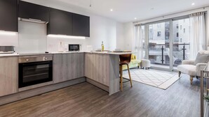 Una cocina moderna con horno y microondas integrados, un comedor con una silla amarilla y un ventanal con cortinas.