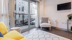 Una sala de estar moderna con un sofá, un sillón, un televisor y vistas a través de un ventanal.
