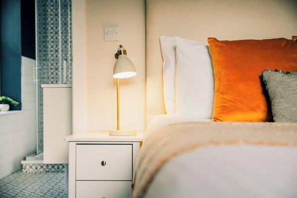 Un lit bien fait, avec des oreillers, une lampe de chevet et une table de nuit dotée d’un tiroir.