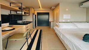 Habitació d'hotel petita amb cuineta, un llit, una cadira i una catifa a ratlles.