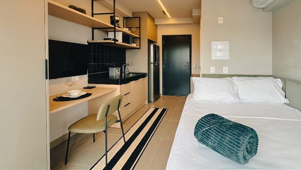 Habitació d'hotel senzilla amb un llit, escriptori, cadira i petita cuina.