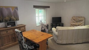 Una sala de estar con una mesa de madera, sillas estampadas, un sofá, un televisor y una ventana con cortinas.