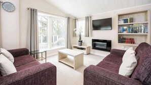 A modern living room with two purple sofas, a coffee table, a flat-screen TV, and a bookshelf.