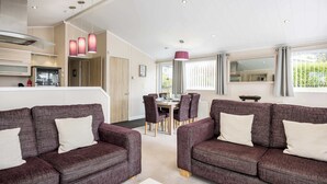 A modern living room with two dark sofas, a dining area with a table and chairs, and a kitchen with a built-in stove.