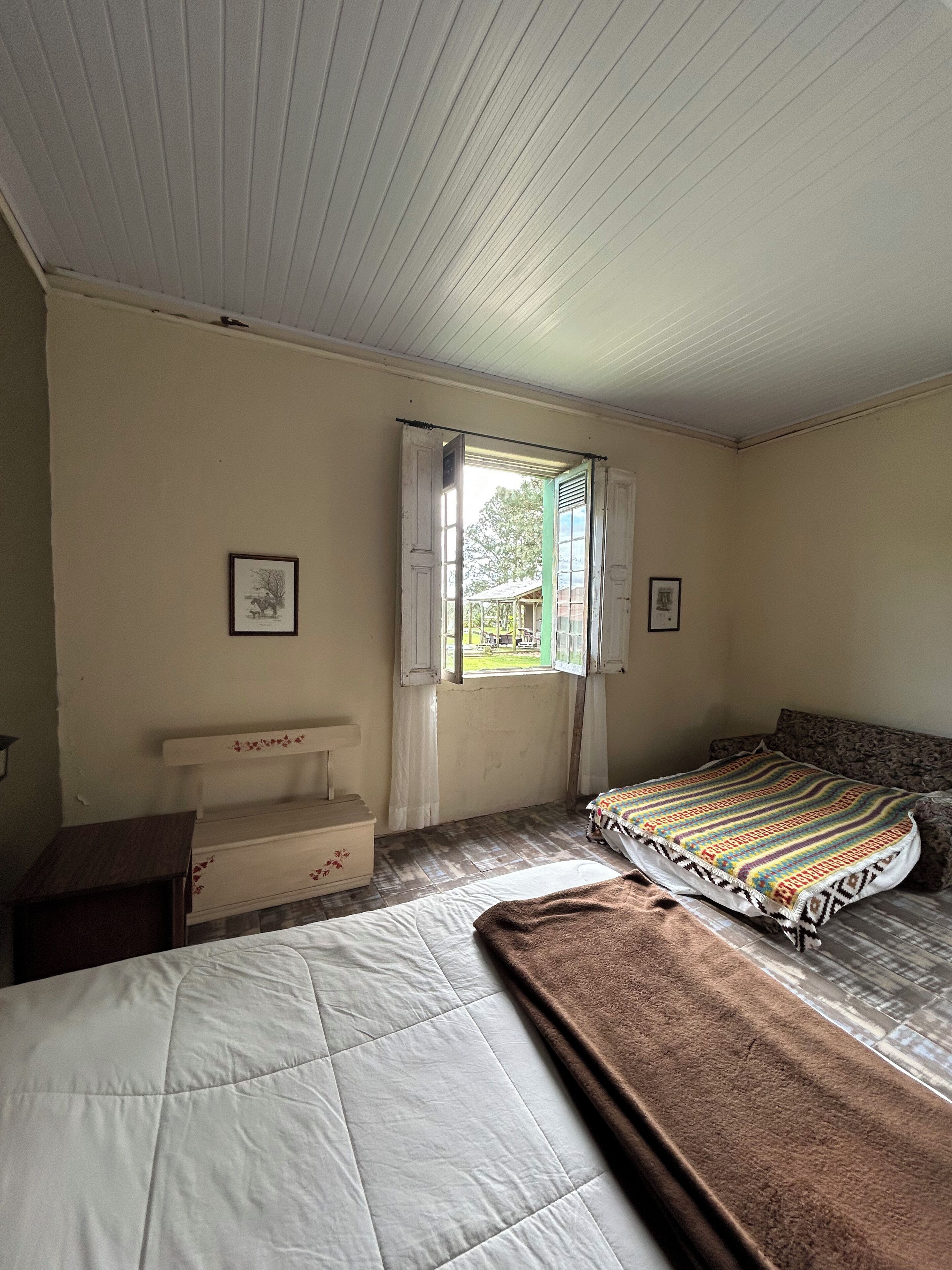 Um quarto com uma cama, um banco e uma janela com cortinas.