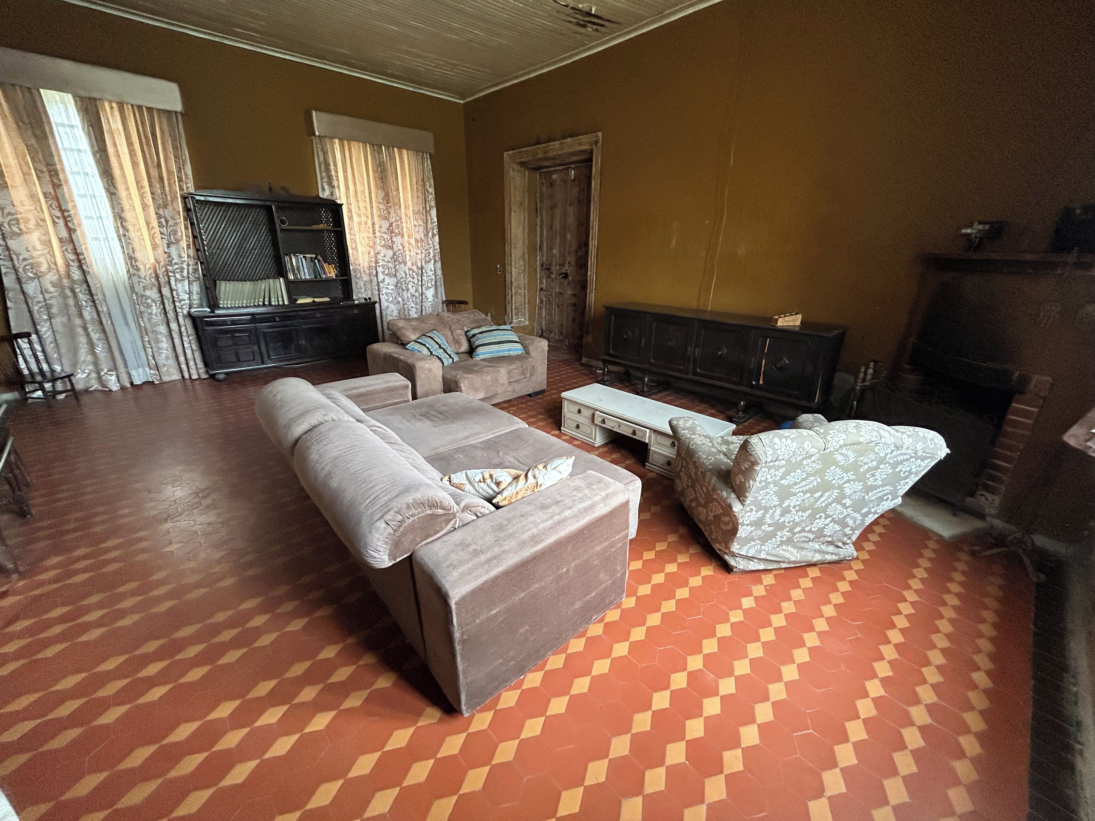 Uma sala de estar com sofá, poltrona e televisão. Há uma lareira e um armário ao fundo.