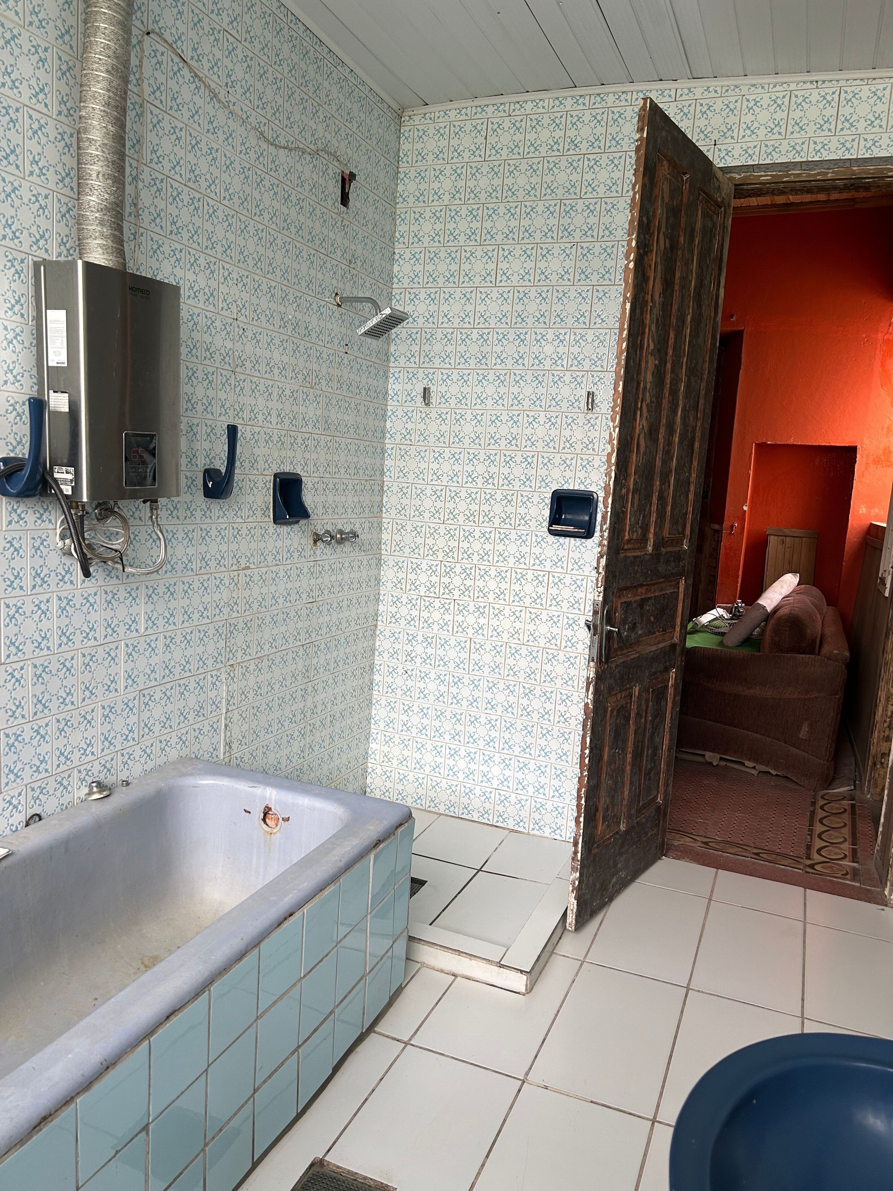 Un baño con bañera, ducha e inodoro. Una puerta de madera da paso a otra habitación.