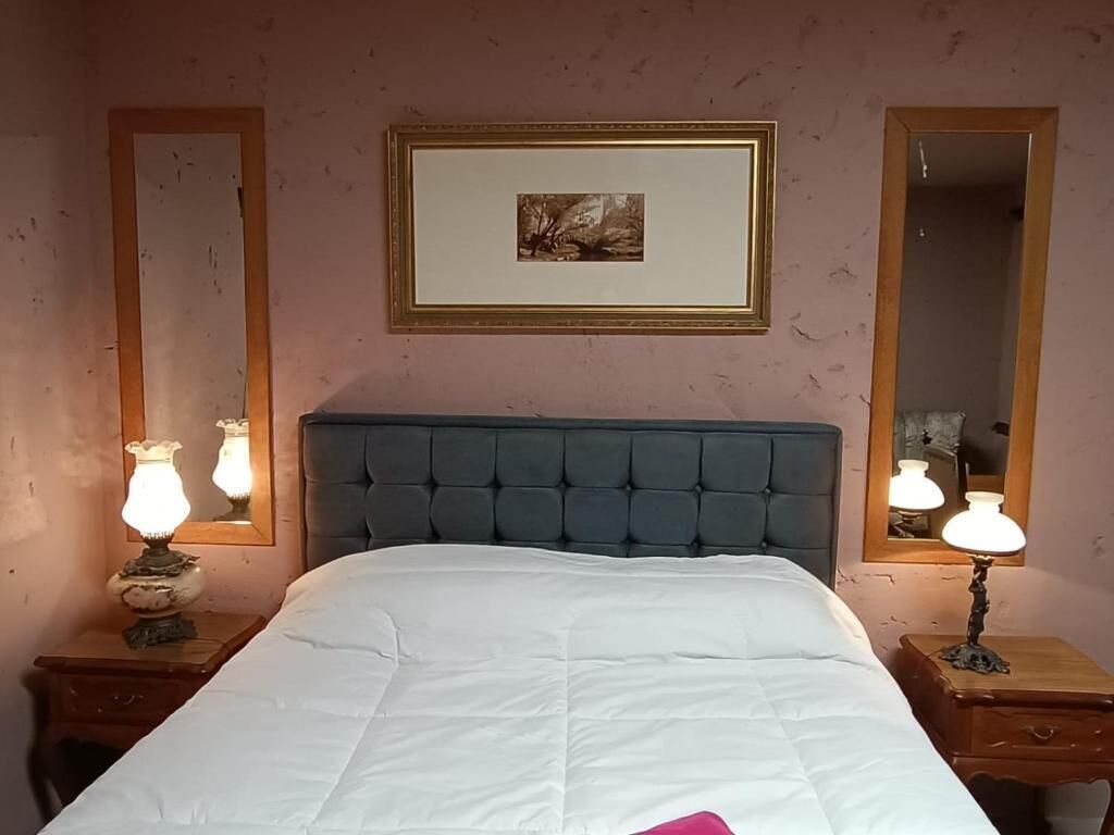 A neatly made bed with a white comforter and a pink accent pillow, flanked by two bedside tables with lamps.