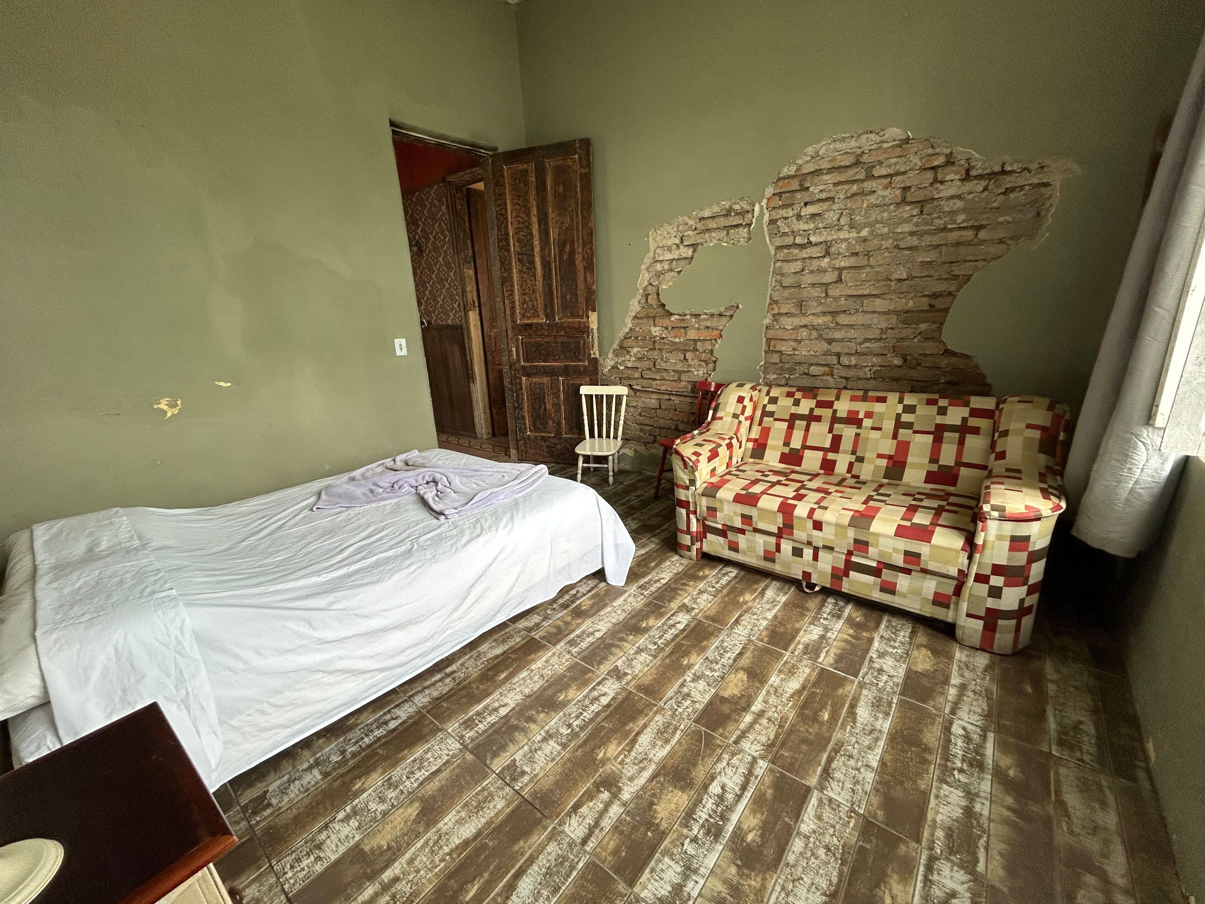 Quarto com uma cama, um sofá estampado, piso de madeira e parede de tijolos.