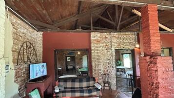 A rustic interior with exposed wooden beams, a brick wall, a checkered sofa, a television, and a billiards table.