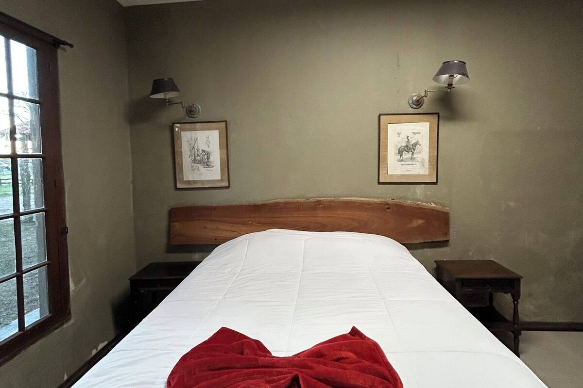 Habitación de hotel con una cama grande, dos mesitas de noche, una ventana y dos lámparas fijadas a la pared.