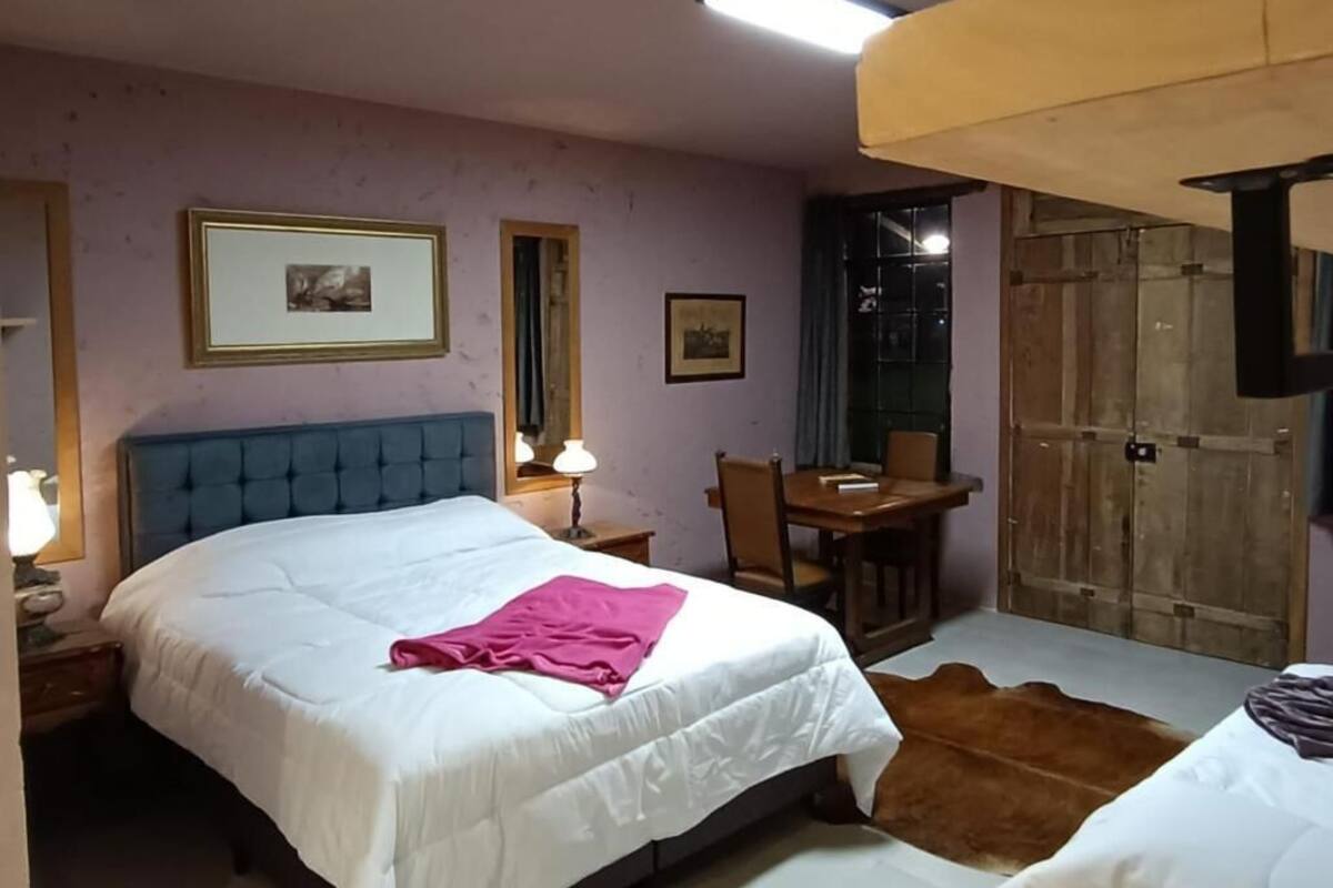 Un dormitorio con cama, mesita de noche, lámpara, cuadros enmarcados, un escritorio de madera, silla y un tapete de cuero de vaca.