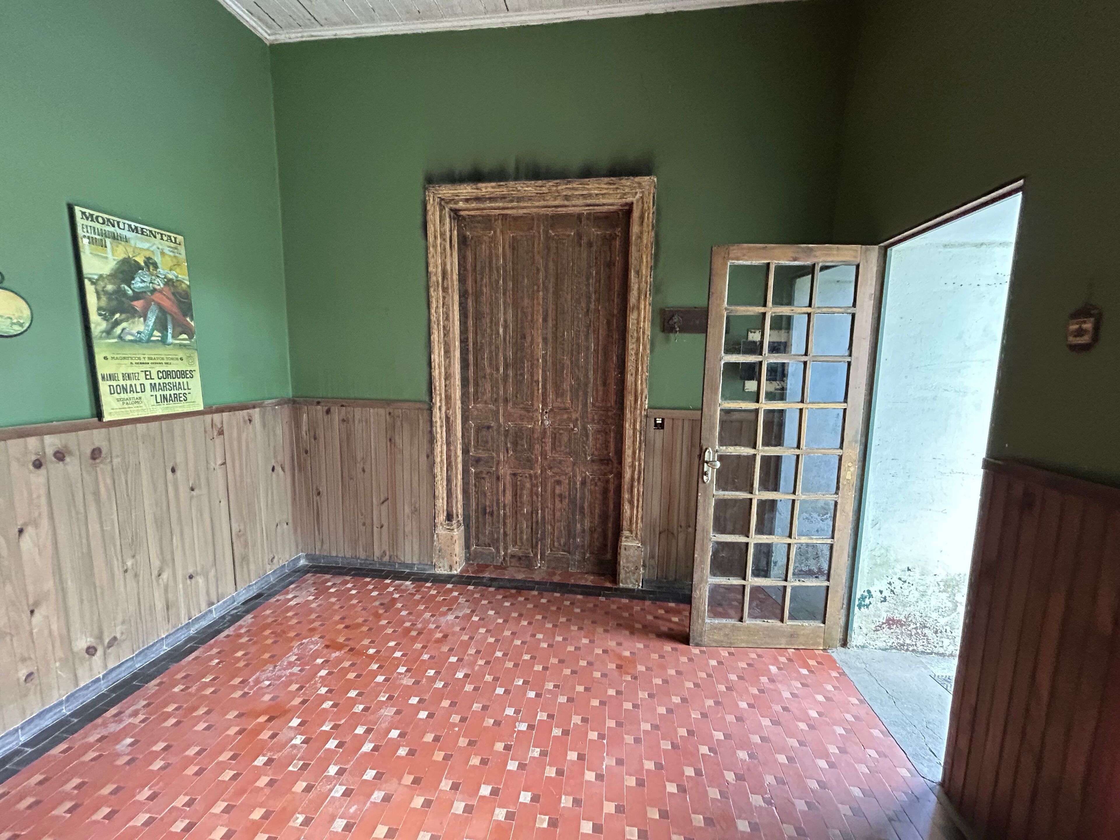 Una habitación con puerta de madera, suelo de baldosas y pared verde.