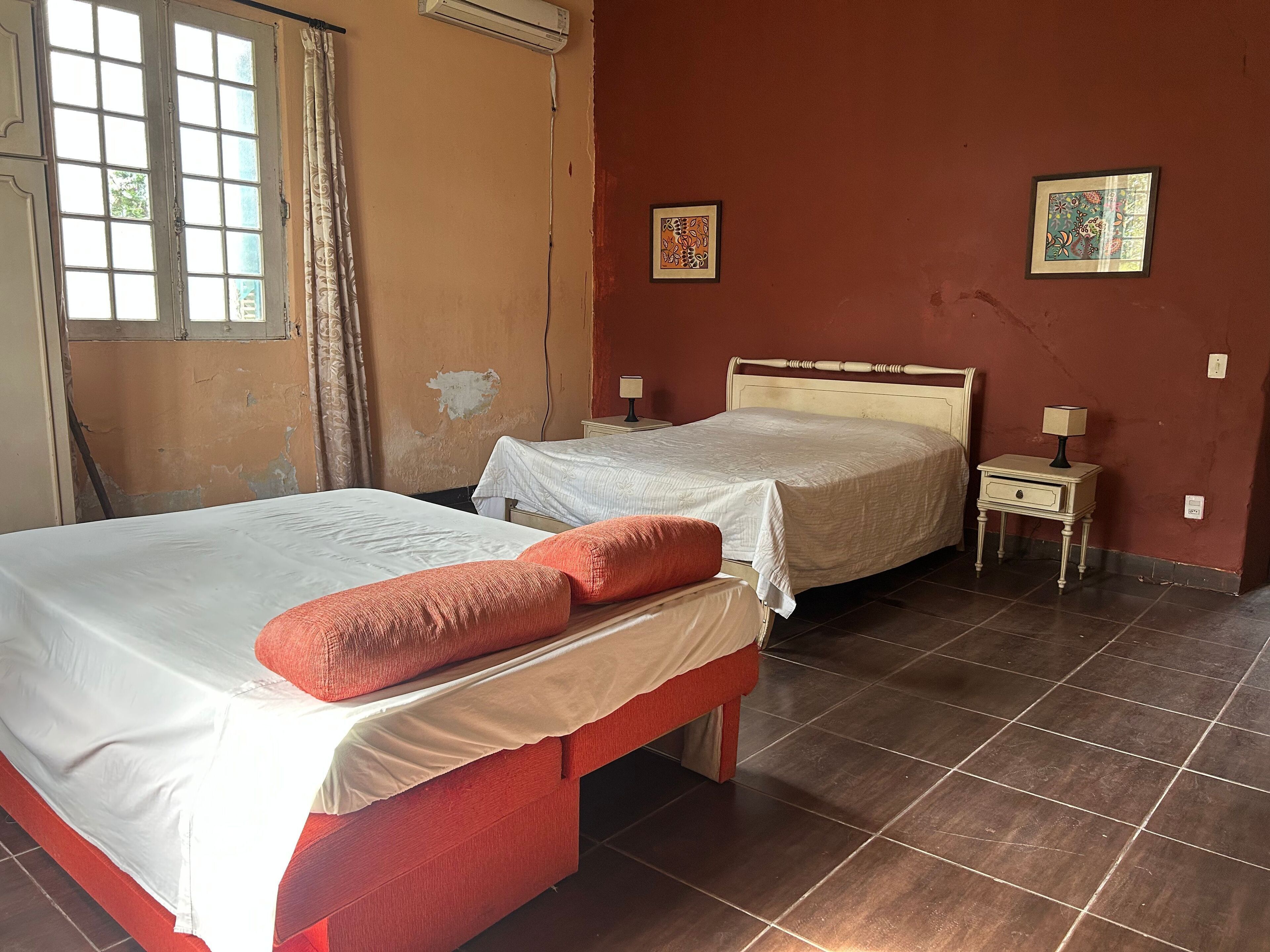 A room with two beds, a small bedside table with a lamp, and a window with curtains.