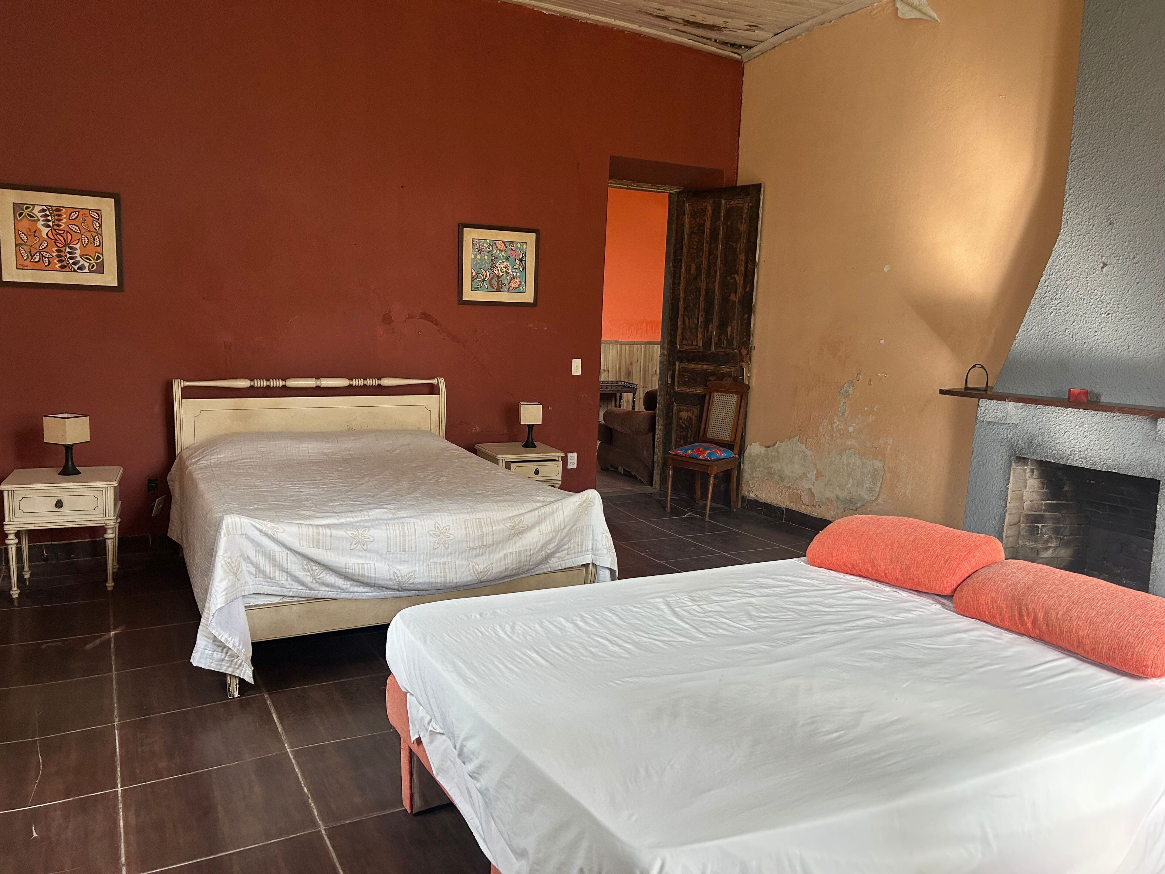 A room with two beds, a wooden headboard, a nightstand with a lamp, a chair, and a fireplace.