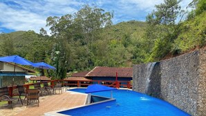 Piscina con muro de piedra y zona de deck con azulejos, sillas y sombrillas.