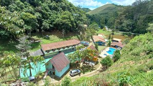 Vista desde la ladera de un resort con varias construcciones, una piscina y abundante vegetación.