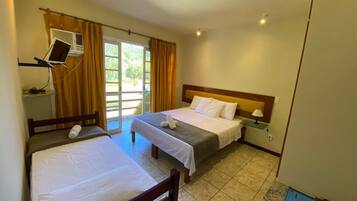 A hotel room with two single beds, a desk, a chair, a small table with a lamp, and an air conditioning unit.