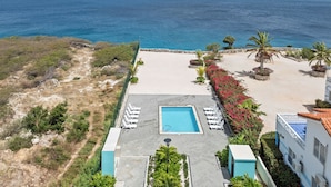 A rooftop pool with a view of the ocean, surrounded by palm trees and a stone wall. - Punta azul 12A Ocean resort  (Sabana Westpunt)