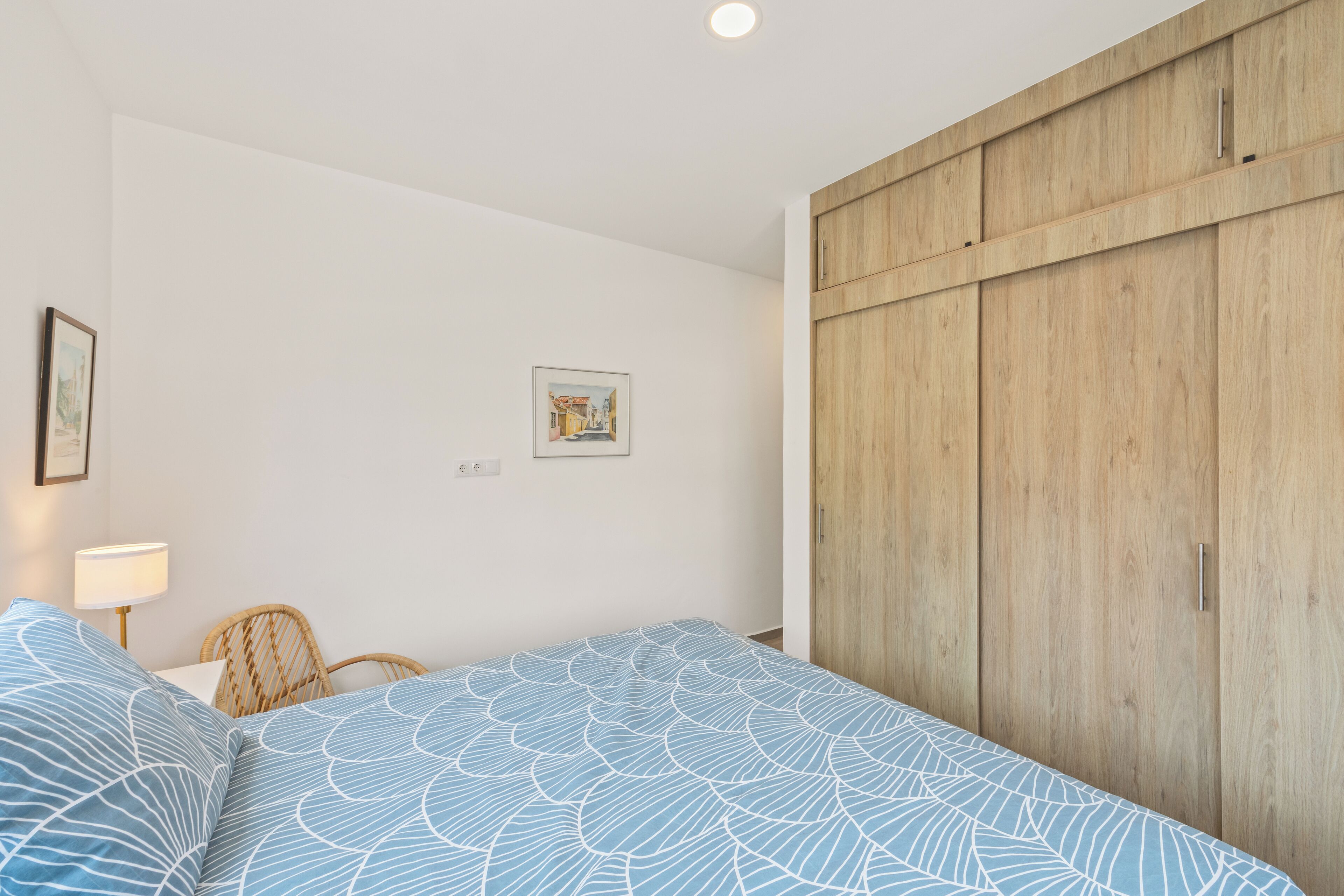 Une chambre à coucher avec un lit, une armoire en bois, une chaise et une lampe fixée au mur.