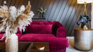 Un salón moderno con un sofá de terciopelo rojo, una mesita auxiliar con una escultura de caballo y plantas decorativas.
