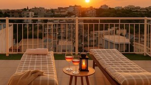 Un balcón con dos camas, una mesa con vasos y un farol, y vistas al atardecer.