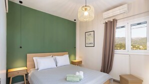 Una cama bien hecha con almohadas, una mesita de noche, una lámpara de noche, una ventana con cortinas y un aire acondicionado instalado en la pared.