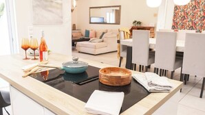 Een moderne keuken met een centraal eiland, een eethoek met stoelen en een woonkamer op de achtergrond.