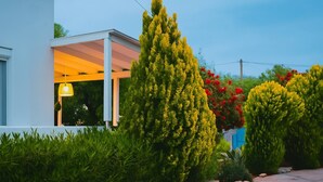 Een modern huis met een overdekte veranda, omringd door goed onderhouden hagen en bloeiende planten.