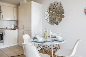 A modern kitchen with white cabinets, a dining table set with white chairs, and a decorative mirror wall.
