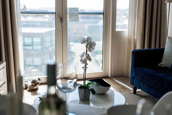 A living room with a large window, a blue sofa, a white coffee table, and a potted orchid.