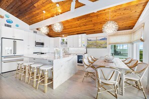 Une cuisine moderne avec des meubles blancs, un îlot en marbre et un coin repas doté de chaises en osier.