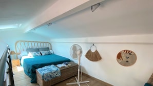 Un dormitorio con cama, mesita de noche, ventilador y adornos en la pared.