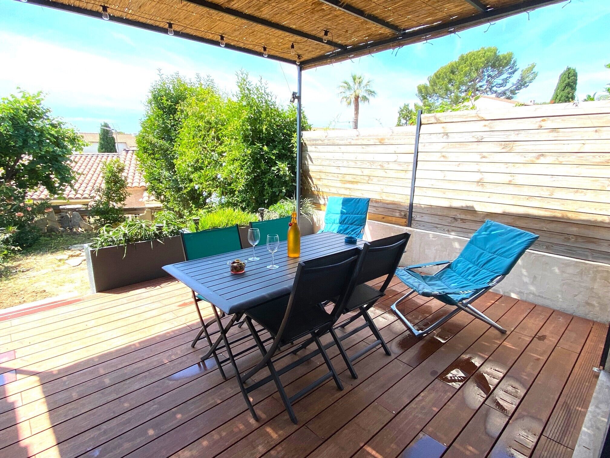 Um pátio externo com mesa e cadeiras, cercado por vegetação e um muro de madeira.