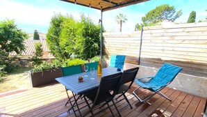 Un patio exterior con mesa y sillas, rodeado de follaje y una cerca de madera.