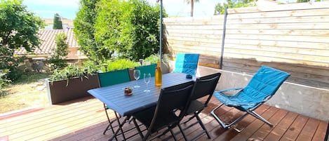 Eine Terrasse im Freien mit Tisch und Stühlen, umgeben von viel Grün und einem Holzzaun.