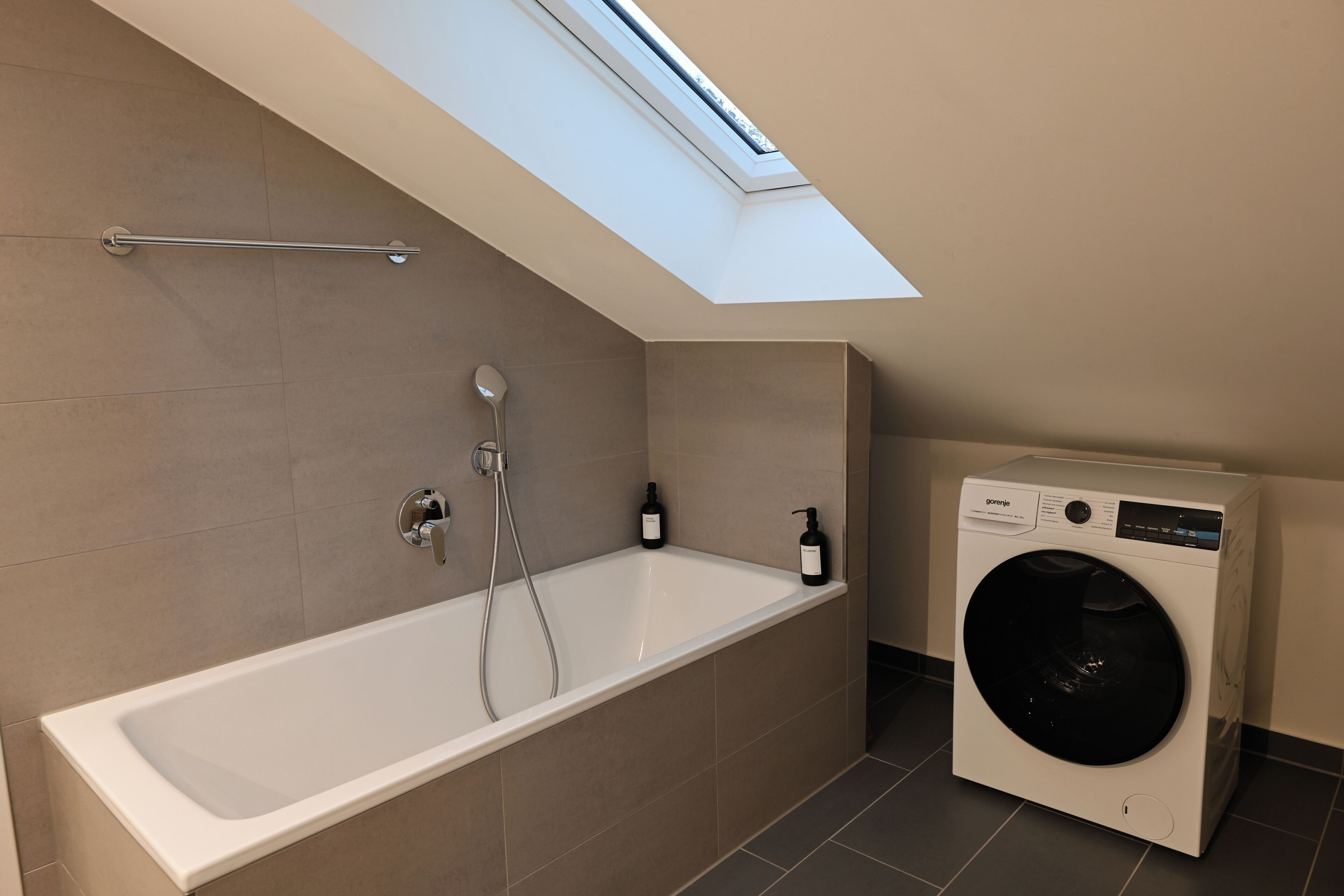 Ein modernes Badezimmer mit Oberlicht, Badewanne und einer Waschmaschine mit Frontlader.
