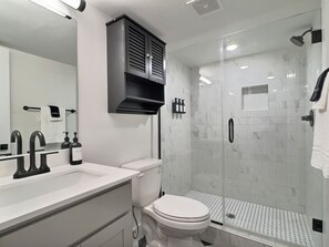 A modern bathroom with a white sink, black faucets, a white toilet, and a glass-enclosed shower area. - Tranquil Getaway w/ Pool & Extra Large Balcony (Birmingham)