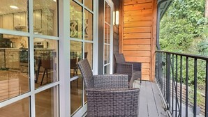 Um deck de madeira com cadeiras de vime e uma porta de vidro que dá para uma cozinha.