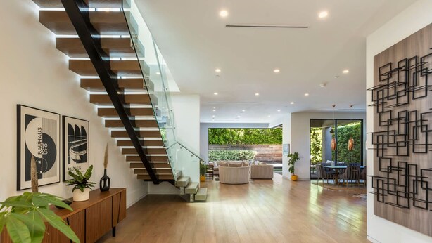 Um interior moderno com escada, piso de madeira e área de jantar com iluminação natural.
