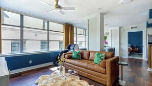 A living room with a brown leather sofa, a fur rug, a ceiling fan, and large windows.